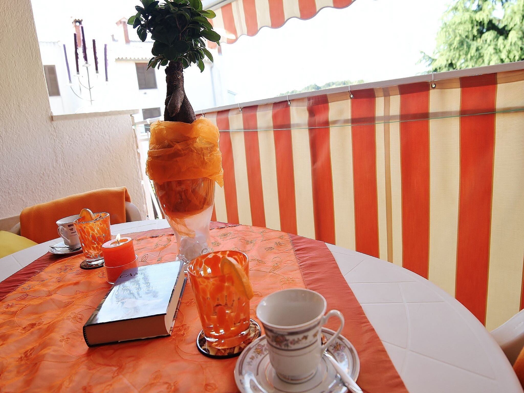 A table with a book, a glass with a lemon slice, a candle, and a cup on a tablecloth.