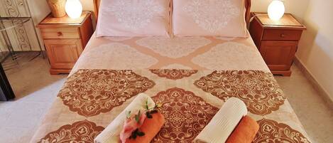 A neatly made bed with patterned bedding, two bedside tables with lamps, and a vase with flowers on one table.
