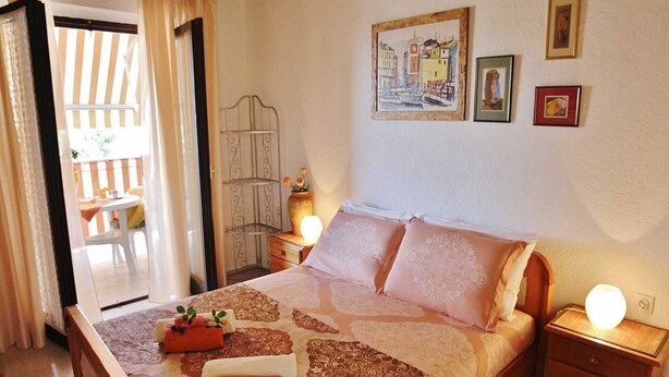A bedroom with a bed, bedside tables, a nightstand, a chair, a table, and a window with curtains. - SEA Studio with Balcony (gornji) (Rovinj)