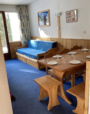 Enjoy a warm and inviting space with a dining table for four, a comfortable sofa, and a large window offering a view of the surrounding greenery.