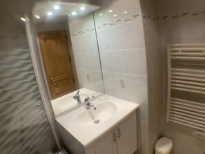 Bathroom features a large mirror above a sink with two faucets, surrounded by light-colored tiling.