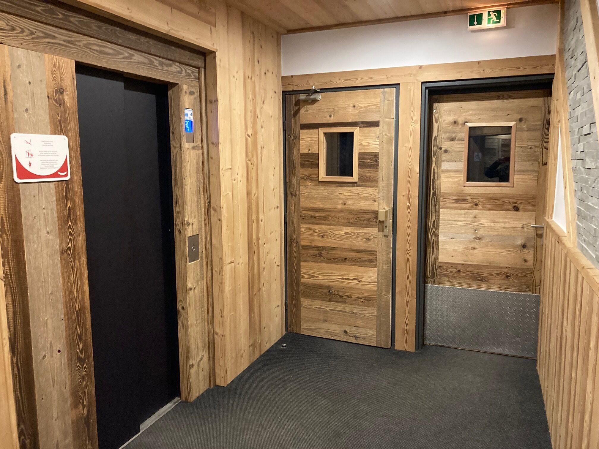 A wooden interior hallway with two doors, one with a small window and a sign, and a textured carpet.