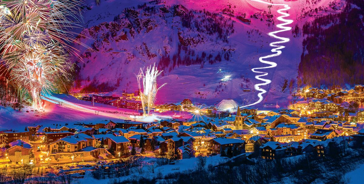 Ein schneebedecktes Dorf mit beleuchteten Gebäuden und einer Skipiste.