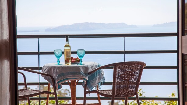 A balcony with a table set for two, featuring a bottle and glasses, overlooking a body of water with distant land. - Quinta do Santo by LovelyStay (Santa Cruz)