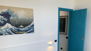 A hotel room with a bed, a painting of waves, a blue door, and a bathroom visible through an open door. - Villa Laura PT - directly by the sea (Pizzo)