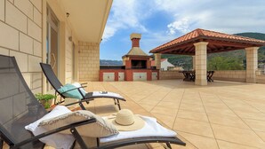 A patio with two lounge chairs, a sun umbrella, a grill, and a view of a mountain. - Mondo Room 1 - One Bedroom Apartment, Sleeps 2 (Mokosica)
