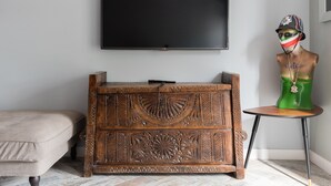A room with a large flat-screen TV mounted on the wall, a wooden cabinet with intricate carvings, a green sculpture on a small table, and a beige sofa.