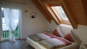 A bedroom with a wooden ceiling, a bed with patterned bedding, a bedside table, and a window with sheer curtains. - family friendly and for nature lovers (Weinheim)