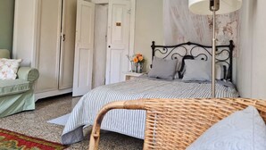A bedroom with a bed, a nightstand, a wicker chair, a wardrobe, and a lamp. - Historic house lovingly furnished in original vintage style (Cesio)