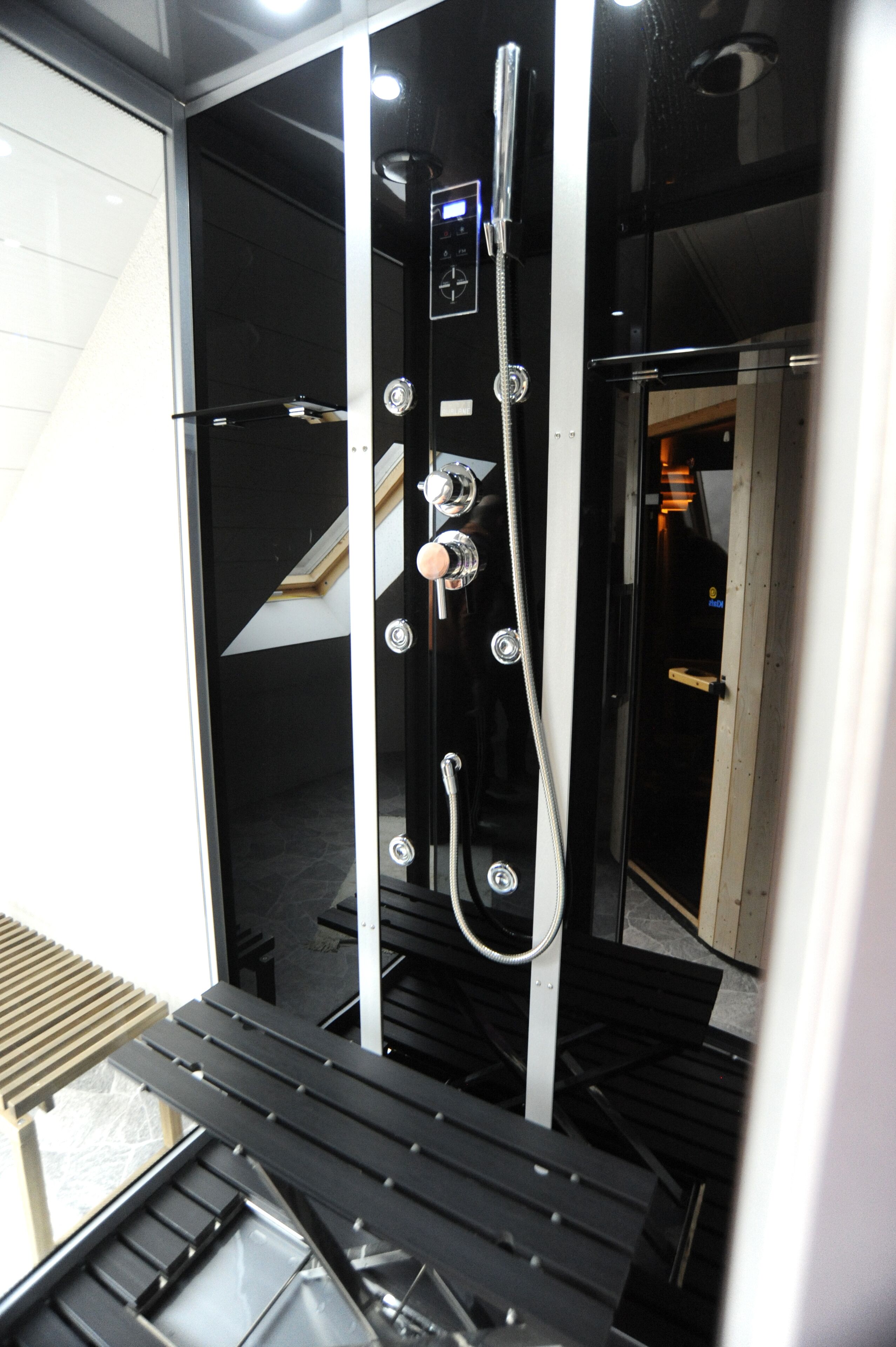 Un espace douche moderne doté d’un panneau de commande, d’un pommeau de douche à main et d’une porte en verre.