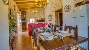 Uma área de jantar com mesa de madeira posta para quatro pessoas, um candelabro e paredes de pedra rústica.