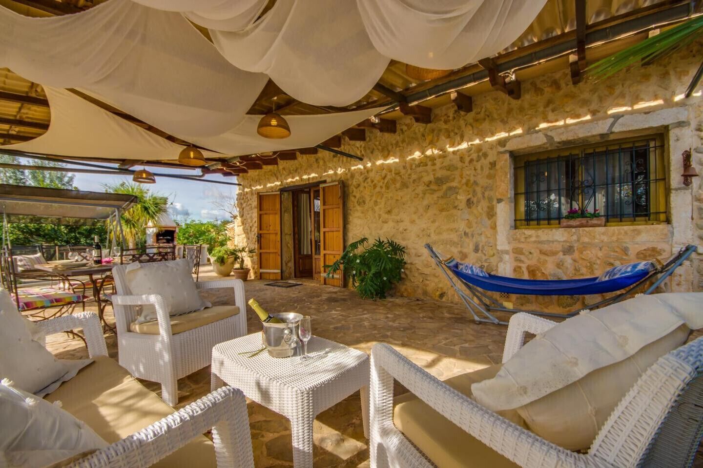 A cozy outdoor seating area with wicker furniture, a hammock, and a stone wall backdrop.