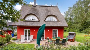 Une maison avec un toit de chaume, des murs rouges et un jardin aménagé avec du mobilier d’extérieur.