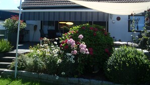 Ett hus med ett tak täckt av takpannor, en inglasad uteplats och en trädgård med olika sorters blommor.