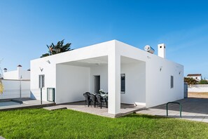 Une maison moderne, blanche, dotée d’un patio abrité, d’une piscine et surplombée d’un ciel d’un bleu éclatant.