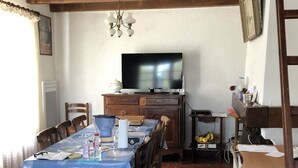 Un coin repas avec une table recouverte d’une nappe bleue, des chaises en bois et un téléviseur posé sur un meuble en bois.
