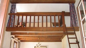 Une chambre à coucher aménagée dans les combles, avec un plancher en bois, un lit superposé, une échelle et un lustre.