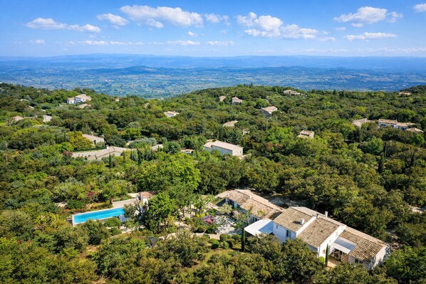 Un quartier résidentiel composé de plusieurs maisons, entouré d’une végétation luxuriante, avec une piscine et une vue sur des paysages lointains.