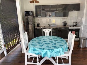 A compact kitchen with modern appliances, a dining table with a patterned tablecloth, and a view through a window with blinds. - bungalow the box lace (Le diamant)