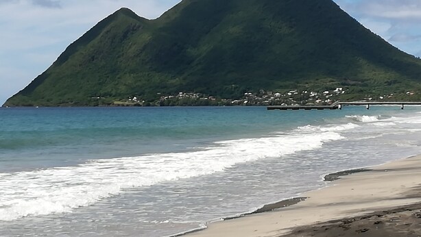 A beach with a mountain in the background and a small settlement visible on the shore. - bungalow the box lace (Le diamant)