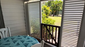 A covered porch with a table and chairs, a view of a garden through open shutters. - bungalow the box lace (Le diamant)