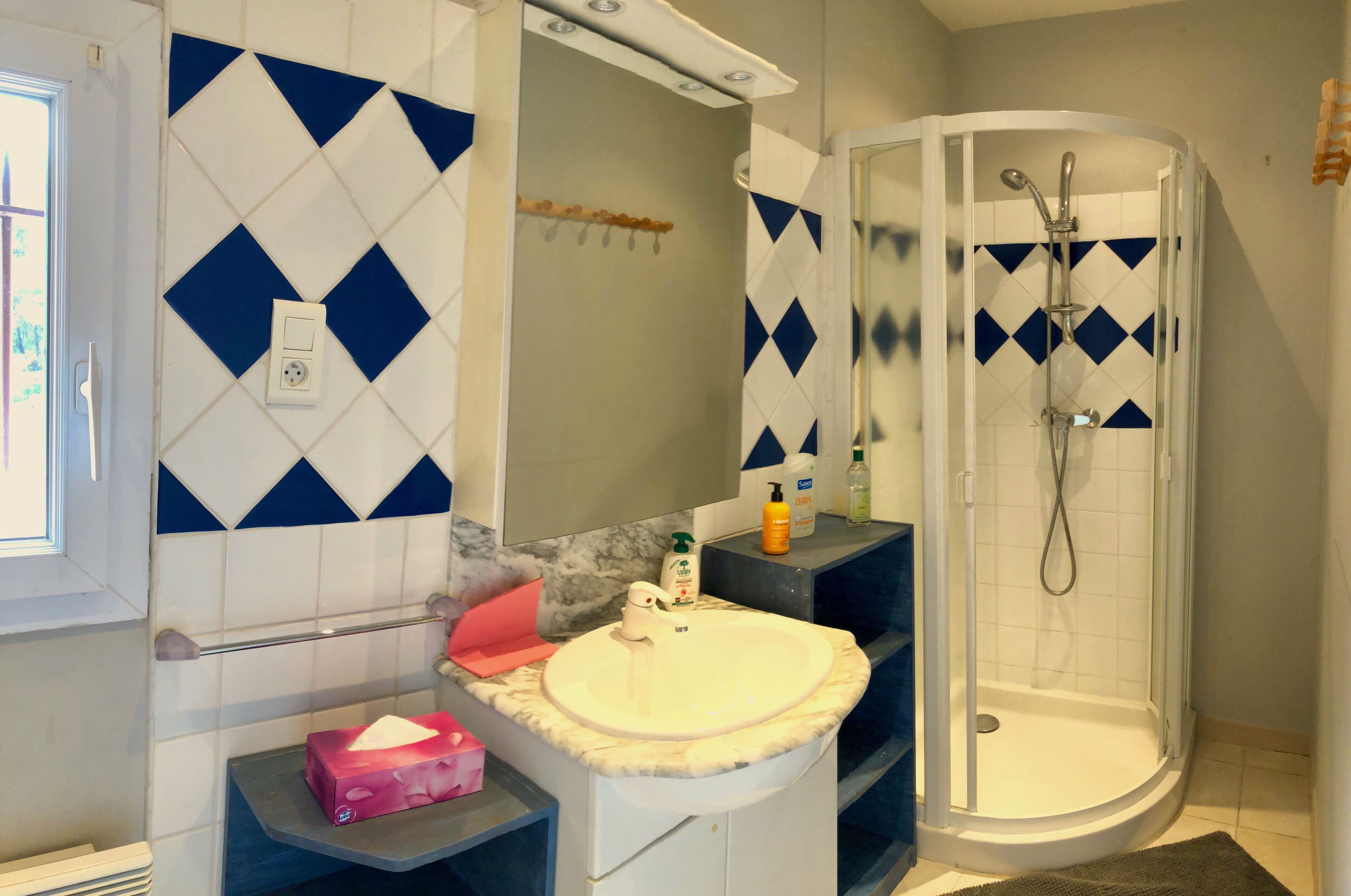 Casa de banho com uma pia branca, chuveiro e azulejos com padrão de losangos azuis.