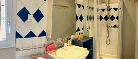Casa de banho com uma pia branca, chuveiro e azulejos com padrão de losangos azuis.