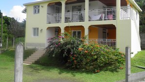A two-story building with balconies, a staircase leading to the entrance, and a garden with flowering plants.