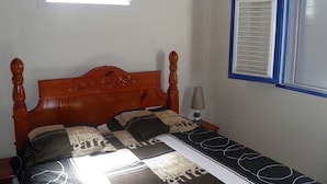 A bedroom with a wooden bed, a bedside lamp, and a window with blinds.