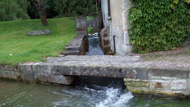 A stone bridge over a flowing stream in a garden setting.