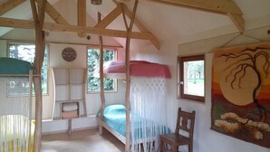 A room with a bunk bed, a chair, a macramé curtain, and a painting on the wall.