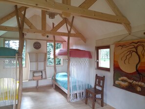 Une chambre avec un lit superposé, une chaise, un rideau en macramé et un tableau accroché au mur.