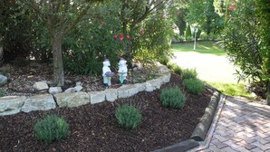 Un jardí amb estàtues decoratives, un marc de pedra, mulç i arbustos petits.