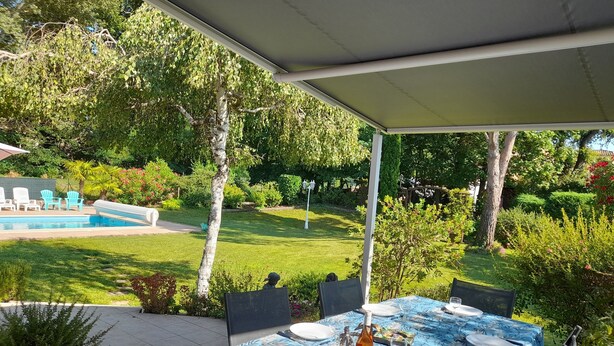 Un pati exterior amb taula preparada per dinar, envoltat de verdura i vistes a una piscina.