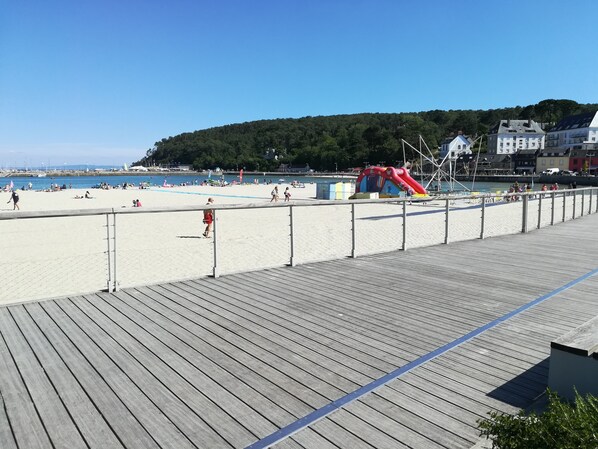 A wooden boardwalk leading to a sandy beach with a playground and buildings in the background. - Quiet flat with sea view, 2 bedrooms, free wifi (Crozon)