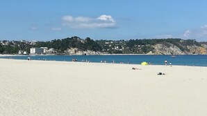 Een breed zandstrand met een helderblauwe lucht en een rustige zee.