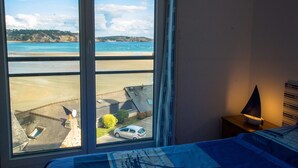 Een kamer met een groot raam met uitzicht op een strand en een parkeerplaats.