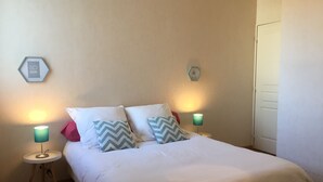 Una cama bien hecha con ropa de cama blanca y dos almohadas, dos lámparas de noche y dos adornos hexagonales en la pared.