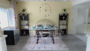 Een eetgedeelte met een glazen tafel, stoelen, een patroonrijk vloerkleed en een klok aan de muur.