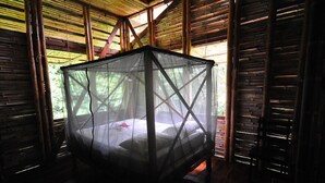 A room with a bed under a mosquito net, wooden walls, and a window with a view of greenery. - Casa Piña,  Bamboo Rainforest Beach House (Cabo Matapalo, Peninusla Osa)
