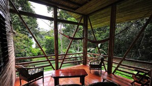 An open-air wooden deck with a view of lush greenery, a wooden table, and two chairs. - Casa Piña,  Bamboo Rainforest Beach House (Cabo Matapalo, Peninusla Osa)