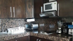A kitchen with dark wooden cabinets, a granite countertop, a microwave, a toaster, and a blender. - Newly Renovated Suite With Beautiful View Of Ocean (Cancún)