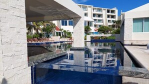 A swimming pool area with clear blue water, white buildings, and palm trees in the background. - Newly Renovated Suite With Beautiful View Of Ocean (Cancún)