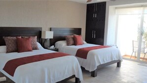 A hotel room with two beds, a dark headboard, a nightstand with a lamp, and a sliding glass door to a balcony. - Newly Renovated Suite With Beautiful View Of Ocean (Cancún)