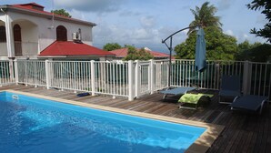 Ein Schwimmbecken mit Holzterrasse, weißem Zaun und Liegestühlen.