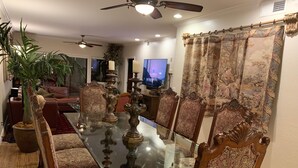 A dining area with a glass-top table surrounded by ornate chairs, a potted plant, and a television in the background. - PRIME LOCATION-GOLF, OLD TOWN, HIKE & BIKE, SPRING TRAINING, SHOPPING... (Scottsdale)