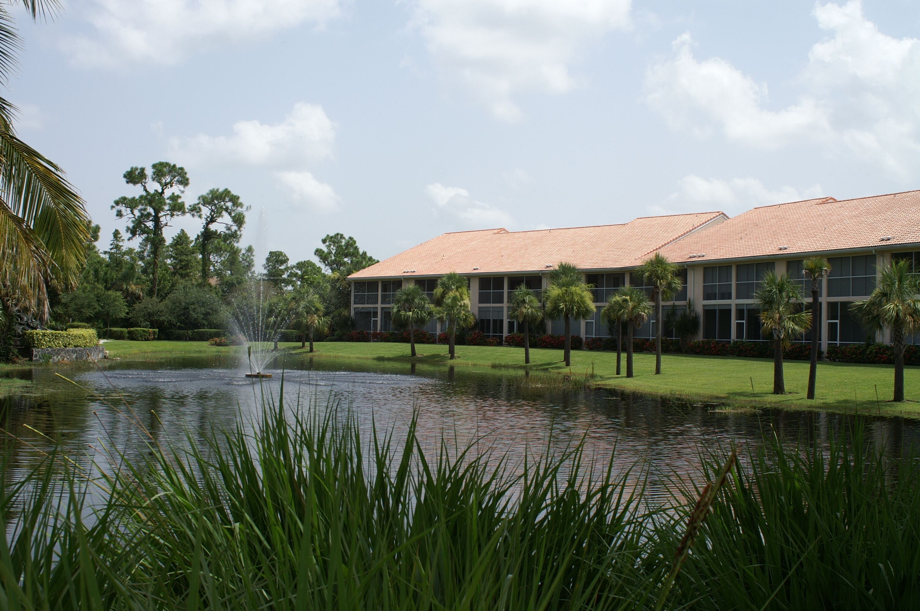 A building with a tiled roof, surrounded by a well-maintained lawn and palm trees.