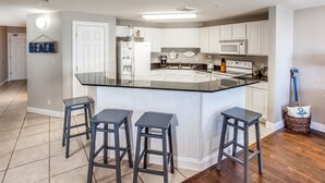 A modern kitchen with white cabinets, a black countertop, and three bar stools. - Calypso401-west
Beachfront (Panama City Beach)
