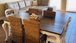 A dining area with a wooden table and wicker chairs, a sofa, and a ceiling fan. - Calypso401-west
Beachfront (Panama City Beach)