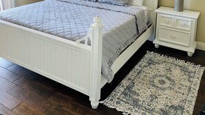 A bedroom with a white bed, two bedside tables with lamps, a ceiling fan, a patterned rug, and a window with curtains. - Calypso401-west
Beachfront (Panama City Beach)